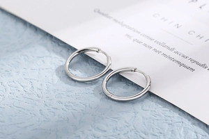 Detailed close-up of silver stainless steel hoop earrings on minimalist textured background