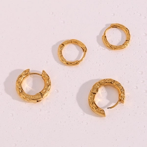 Detail of golden hammered hoop earrings with irregular texture on pink water surface