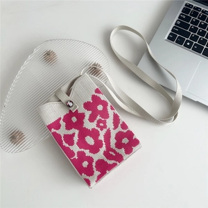 Detailed close-up of knitted mini crossbody phone bag with floral pattern on a glass tray