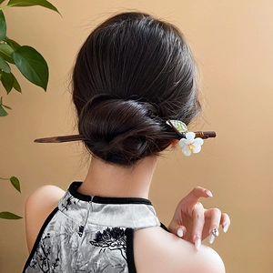 Detailed back view of a Chinese floral hair pin with white petals and green leaves on wood