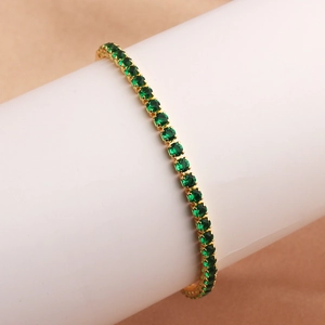 Detailed view of emerald green zircon stones set on a thin gold box chain bracelet
