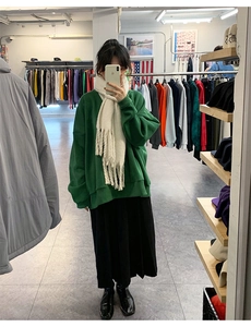 Mirror selfie showing the style of a thick beige tassel scarf with a green sweatshirt