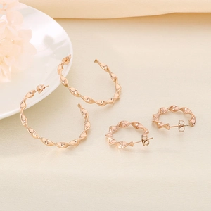 Detail of rose gold twisted C-shaped hoop earrings in large and small sizes on soft fabric
