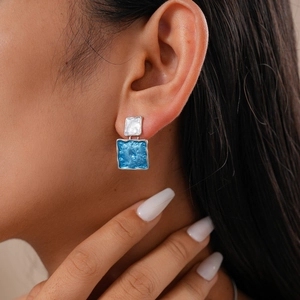Close-up of geometric square earrings in blue and silver on a model's ear