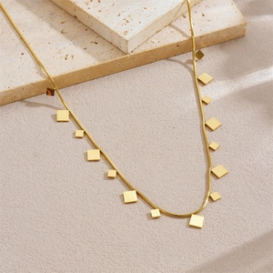 Minimalist gold necklace with geometric square pendants on a beige stone surface