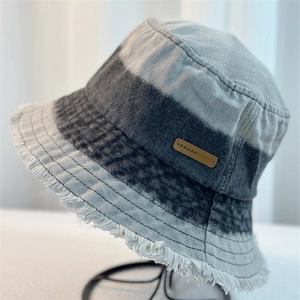 Detail of grey and black denim bucket hat featuring frayed edges and a leather brand label
