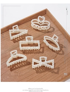 Close-up of six unique pearl hair claw clips on a wooden tray with elegant cream finish