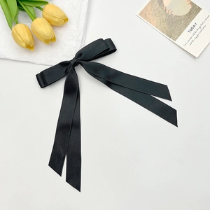 Detail of elegant black satin bow hair clip with long ribbons and smooth fabric texture