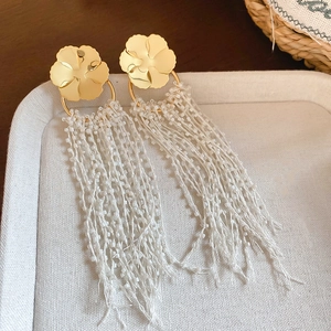 Detail view of golden flower earrings with long white beaded tassels on a white tray