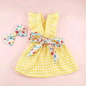Flat lay of yellow plaid pet dress with floral bow accessory on pink background