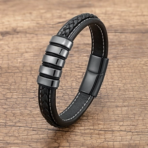 Close-up of black braided leather bracelet with silver metal rings on a wooden base
