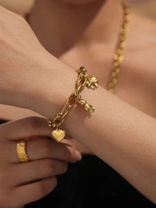 Detail of a gold titanium steel bracelet featuring bear, heart, and clover charms