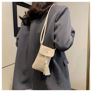 Dettaglio della borsa porta cellulare in paglia intrecciata con nappe su blazer grigio