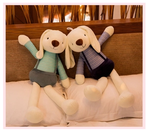 Detail of plush bunny pair in striped outfits leaning against a wooden headboard