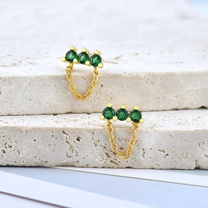 Detailed shot of gold earrings with three green cubic zirconia stones on stone base