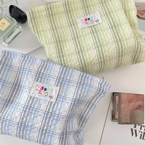 Dettaglio di pochette trucco a quadretti verdi e blu con etichette ricamate