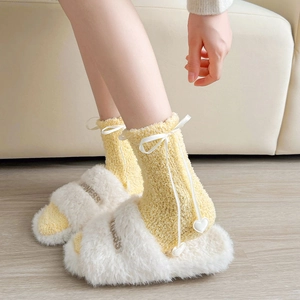 Détail de chaussettes en velours corail avec nœuds et pantoufles douces sur canapé