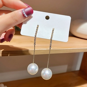 Detailed close-up of C-shaped gold drop earrings with zircon crystals and large pearls