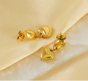 Dettaglio di orecchini a cuore placcati oro 18K su seta champagne e marmo pregiato