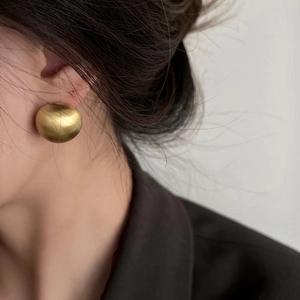 Minimalist golden dome stud earrings with brushed metal finish worn by a model