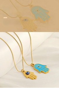Close-up of gold Hamsa Hand pendants with blue Evil Eye and snake chain detail