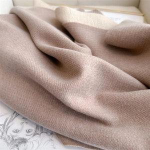 Detailed close-up of soft beige cashmere-like scarf fabric with elegant rolled edges