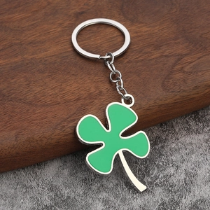 Close-up of green enamel four-leaf clover keychain on wood and stone surface