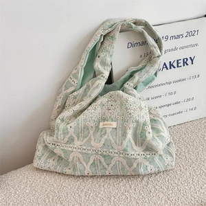Detail of light green canvas shoulder bag with white lace embroidery and fabric handle