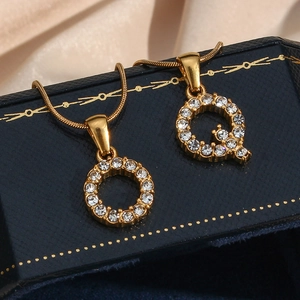 Macro shot of 18K gold plated initial pendants O and Q with crystals on snake chain