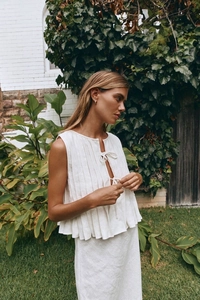 Detail of white sleeveless pleated cotton top with front ties in a garden setting
