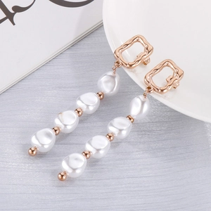 Gros plan de boucles d'oreilles dorées avec perles blanches irrégulières sur fond gris