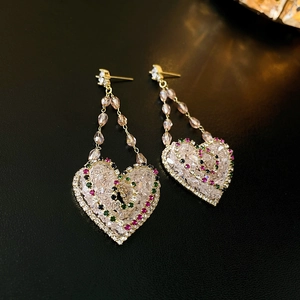 Macro shot of gold heart dangle earrings with sparkling diamonds and colorful gemstones