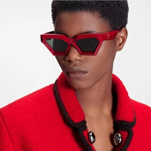 Close-up of red geometric sunglasses with gold temple logo worn with tweed blazer