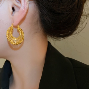 Close-up of 18k gold plated hollow woven hoop earring worn by a model in a dark blazer