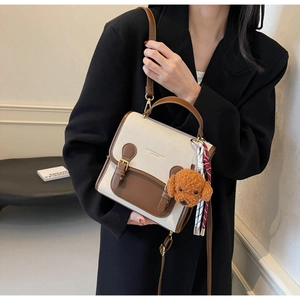 Detail of two-tone beige and brown leather crossbody bag with teddy dog charm on model
