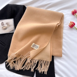 Close-up of camel cashmere-style scarf with fringe and brand label on white bedsheets
