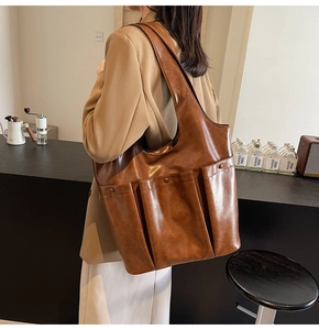 Brown PU leather tote bag with external pockets shown on shoulder in a warm cafe setting
