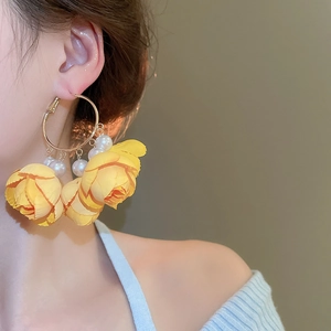 Detail of yellow fabric flowers and pearl fringe hanging from golden metal hoop earrings