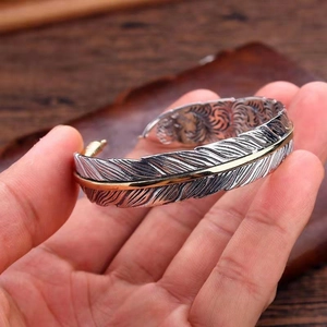 Adjustable retro feather cuff bracelet in silver and gold tones with embossed details