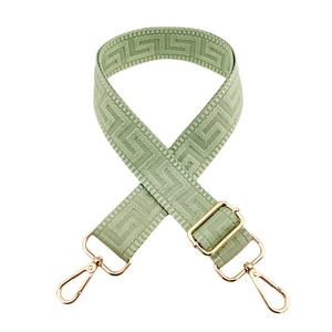Detail of light green bag strap featuring a geometric Greek key pattern and gold hardware