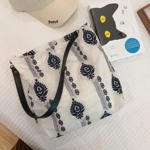 Detail of ethnic blue embroidery on a white linen tote bag with black leather strap