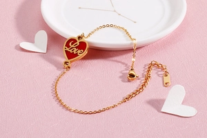 Macro detail of gold stainless steel bracelet with red heart Love charm on ceramic plate