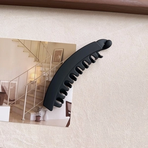 Detailed top view of a large black matte banana clip on a minimalist postcard background