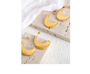 Gros plan de boucles d'oreilles lune dorées sur pierre travertin beige et tissu de soie