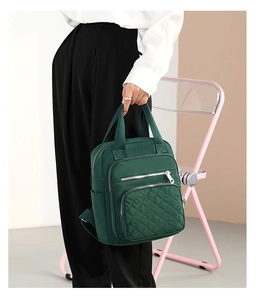 Dark green nylon backpack with quilted diamond stitching held by a model in a studio