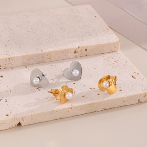 Elegant gold and silver heart pearl earrings set displayed on a natural beige stone pedestal