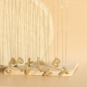 Golden bubble letter pendant necklace with white zircon pavé on beige ceramic plate