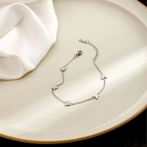 Detailed view of a silver butterfly charm bracelet on a beige ceramic plate