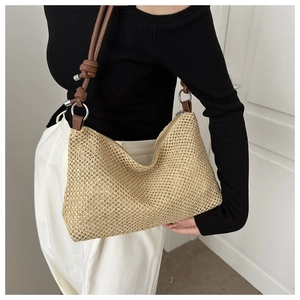 Close-up of woven straw shoulder bag with brown strap and knot detail on a model