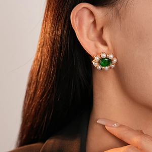 Close-up of pearl flower stud earrings with a green gemstone on model's ear